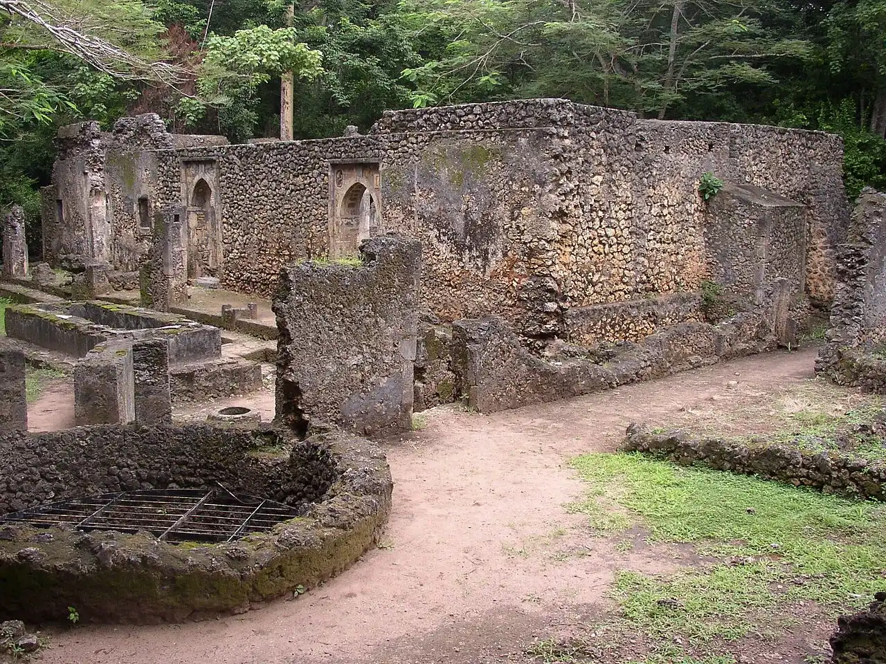 Ruined stone walls and arched openings of the Great Mosque at Gedi, surrounded by trees.