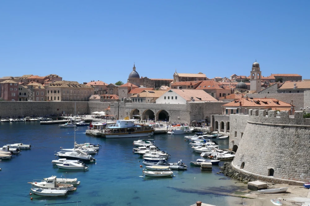 Small boats in Dubrovnik’s old harbour, with stone waterfront buildings, city walls and red roofs.
